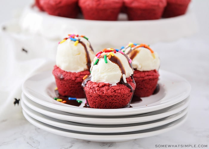 three small red velvet cake mix brownies on a stack of plates and topped with a scoop of ice cream, sprinkles and chocolate syrup