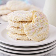 a stack on white cake mix cookies on a plate topped with a white glaze drizzled on top and pastel colored sprinkles
