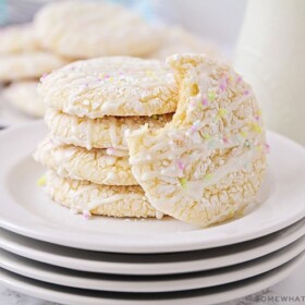a stack on white cake mix cookies on a plate topped with a white glaze drizzled on top and pastel colored sprinkles