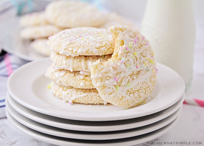 a stack on white cake mix cookies on a plate topped with a white glaze drizzled on top and pastel colored sprinkles