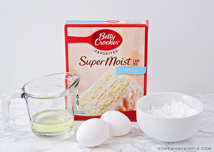 a box of better crocker white cake mix, oil, eggs and a bowl of powdered sugar on a counter