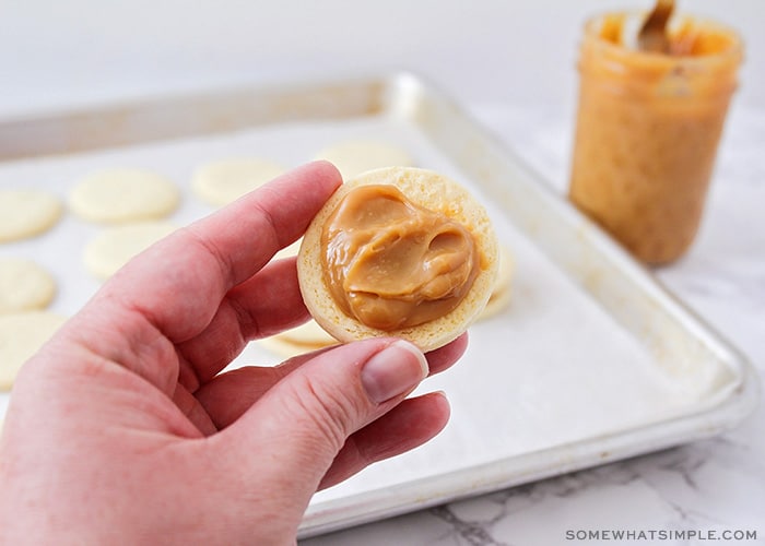una mano sosteniendo una capa de galleta con dulce de leche untado