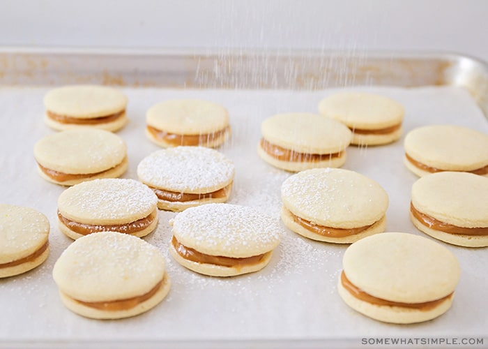 a baking sheet filled with alfajore cookies and powdered sugar is being sprinkled over the top
