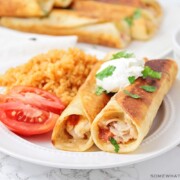 two crispy chicken taquitos on a plate topped with sour cream and a side of rice