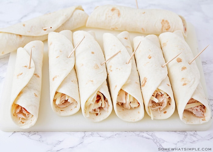 several flour tortillas rolled up that have shredded chicken sticking out and each one has a toothpick stuck in it to keep them from unrolling.