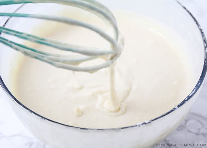 batter in a large clear bowl with a whisk dripping from above