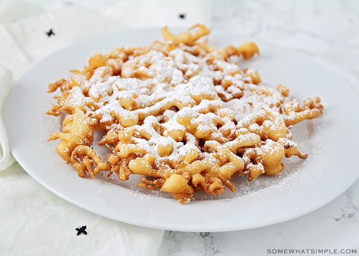 a freshly cooked funnel cake on a plate topped with powdered sugar