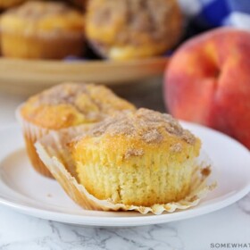 two peach muffins on a white plate with a streusel topping