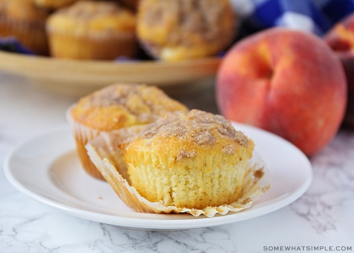 two peach muffins on a white plate with a streusel topping