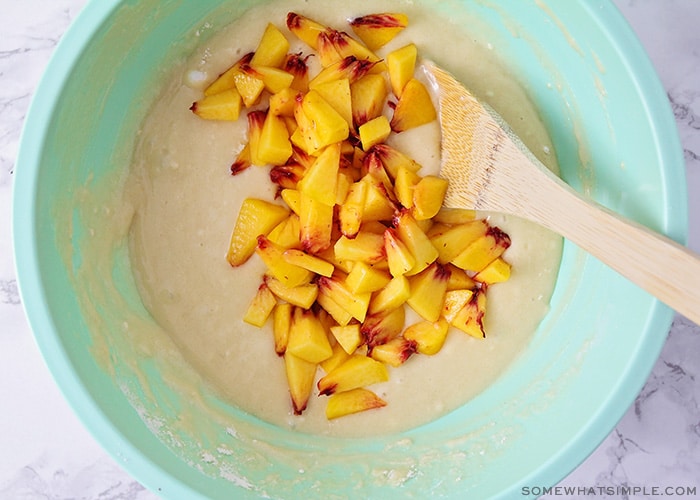 looking down on a bowl filled with muffin batter with a pile of freshly cut peach chunks on top