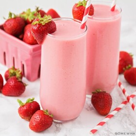 two tall glasses of a strawberry Julius with a whole strawberry sitting on the rim of the glass