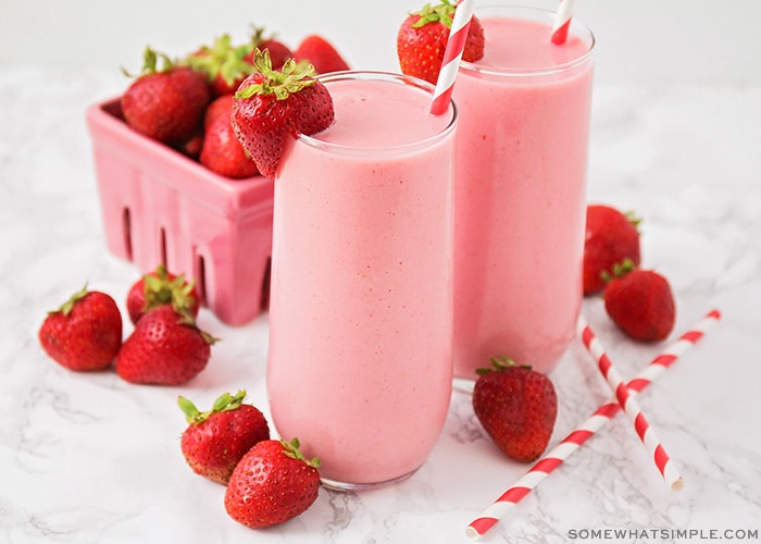 two tall glasses of a strawberry Julius with a whole strawberry sitting on the rim of the glass