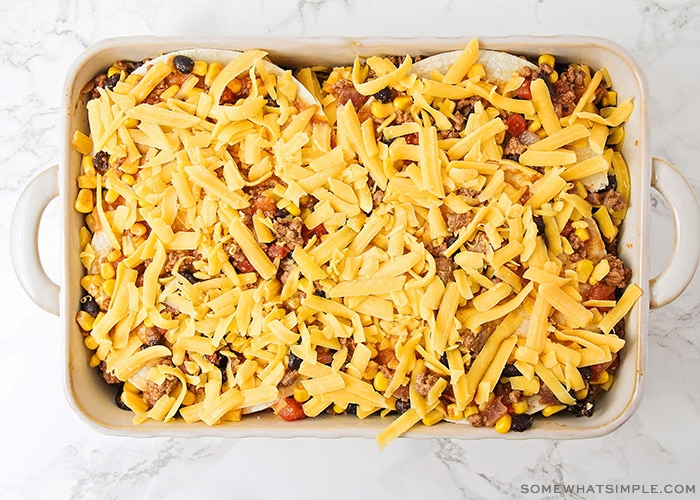 a pan filled with taco casserole and topped with shredded cheese ready to go in the oven