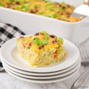 a square of tater tot breakfast casserole with pieces of bell peppers and sausage on a stack on white plates