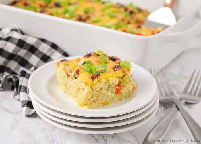 a square of tater tot breakfast casserole with pieces of bell peppers and sausage on a stack on white plates