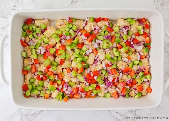 a casserole pan filled with tater tots and a layer of diced onions, green and red bell peppers over the top
