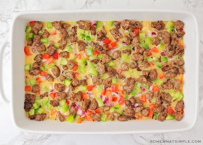 a casserole dish filled with sausage and diced bell peppers with an egg mixture poured over the top