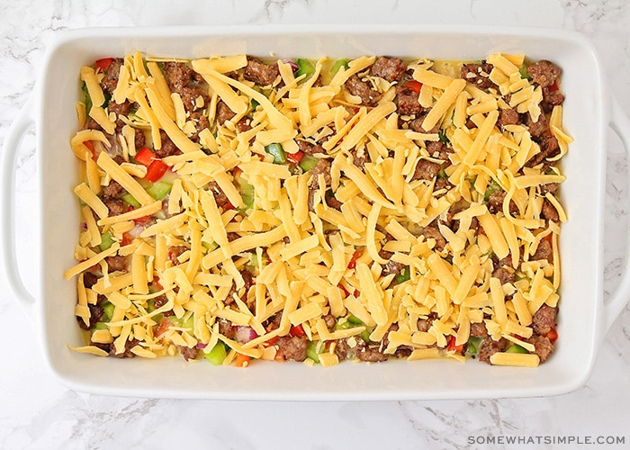 an uncooked tater tot casserole topped with shredded cheese