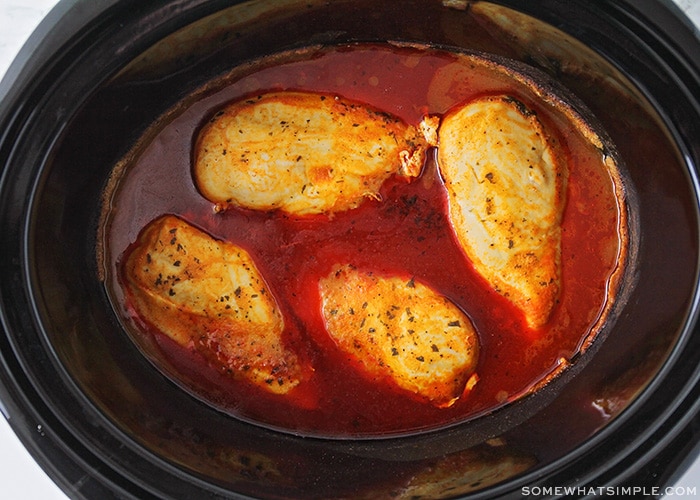 4 chicken breasts cooking in a crock pot with buffalo sauce