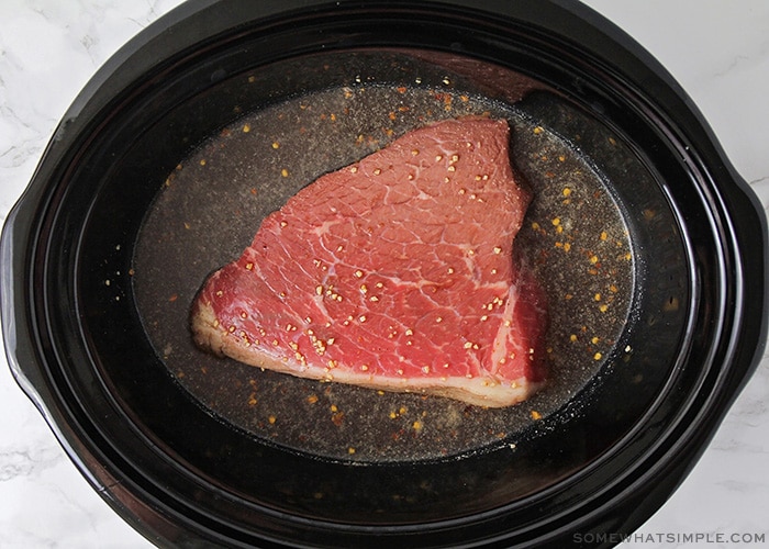 a raw piece of beef in a crock pot with broth