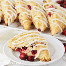 Cranberry White Chocolate Scone plated on a white plate with a serving platter of even more in the background