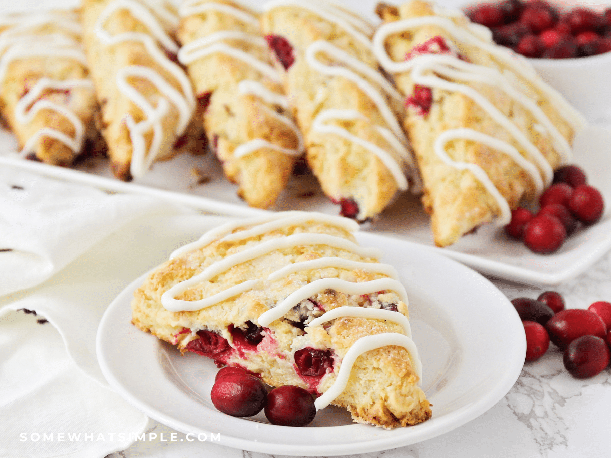 Cranberry White Chocolate Scone plated on a white plate with a serving platter of even more in the background