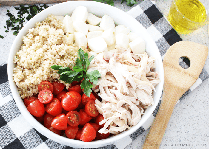 a bowl filled with quinoa, mozzarella cheese balls, shredded chicken and cherry tomatoes