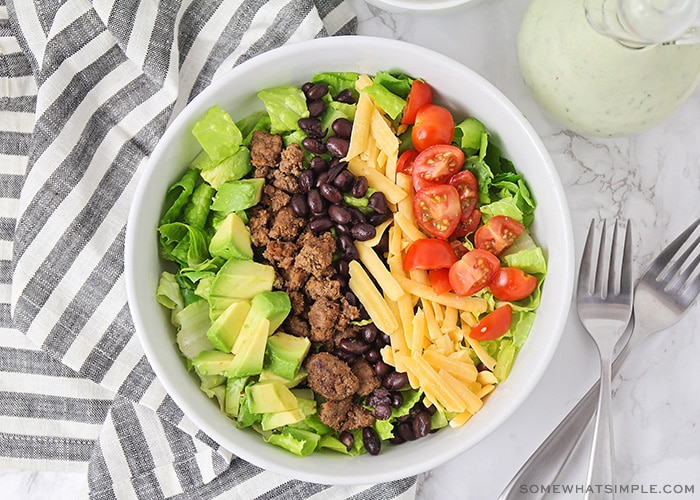 looking down on a salad topped with avocado, ground beef, cheese, beans and tomatoes