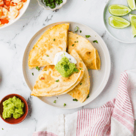 Shrimp Quesadillas plated on a white plate next to limes and guacamole