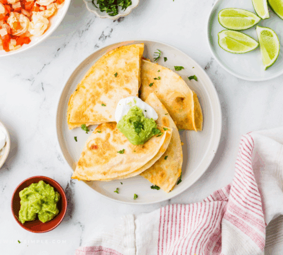 Shrimp Quesadillas plated on a white plate next to limes and guacamole