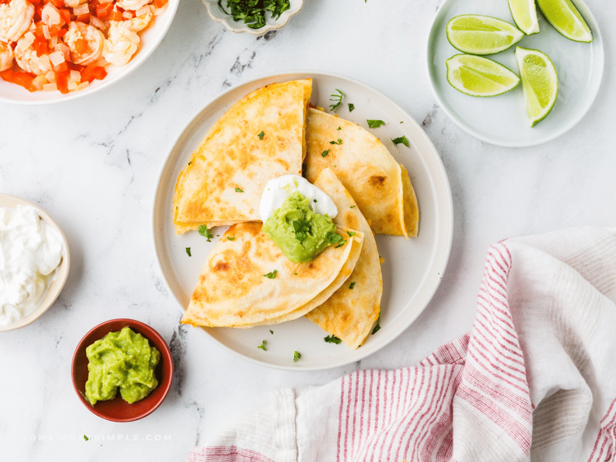 Shrimp Quesadillas plated on a white plate next to limes and guacamole