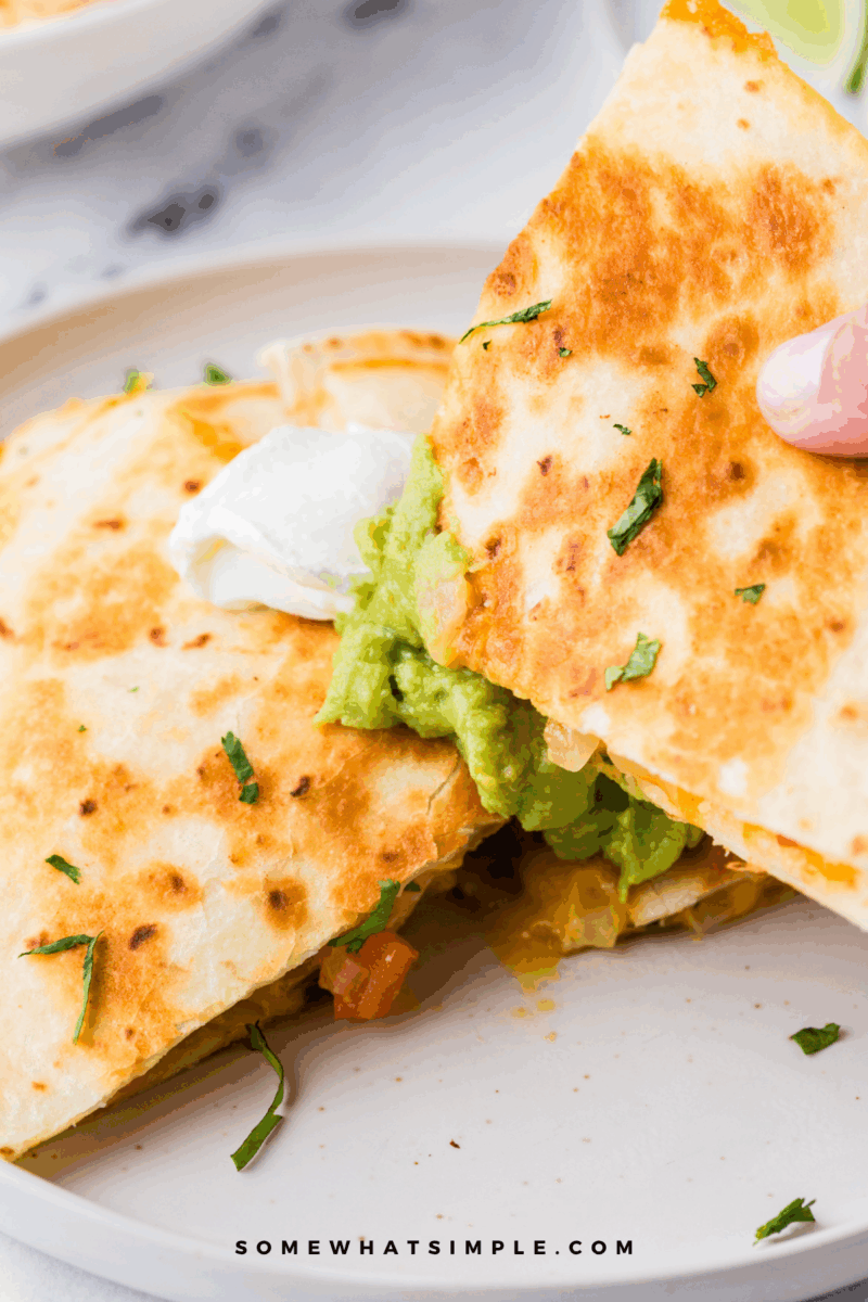 womans hand holding a Shrimp Quesadilla, dipping it into fresh guacamole