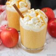 a glass of apple cider topped with whipped cream and caramel