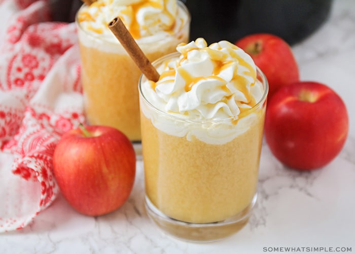 a glass of apple cider topped with whipped cream and caramel