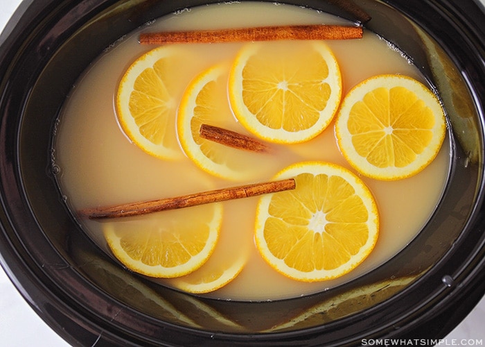 apple cider in a slow cooker with cinnamon sticks and orange slices