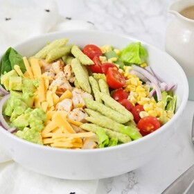 grilled chicken salad with lettuce, cheese, corn, tomatoes, and snap peas in a white bowl
