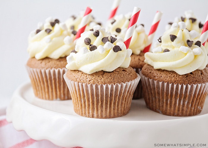 a tray of hot cocoa cupcakes with a cute straw on top