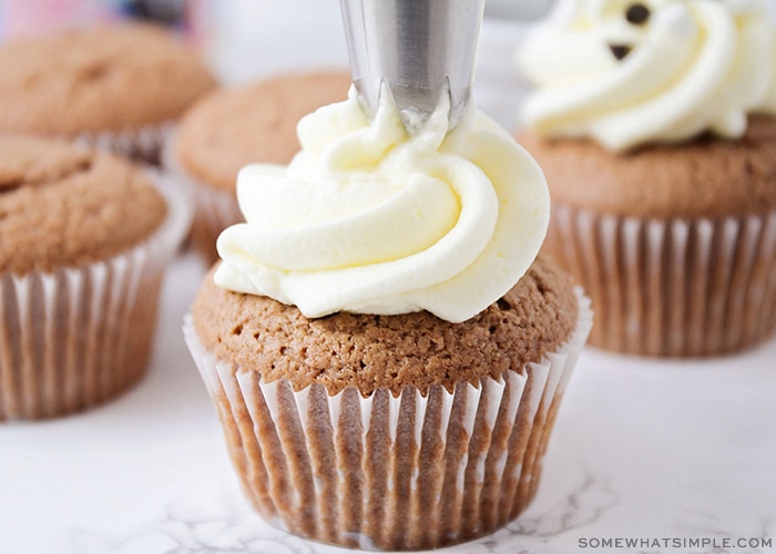 white frosting being piped onto a cupcake