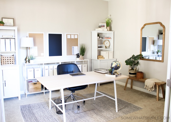 a home office with a desk, rug, mirror and shelves