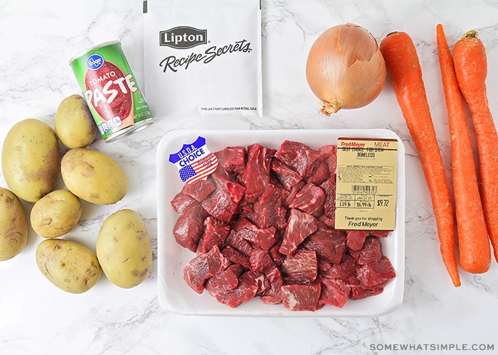 potatoes, an onion, carrots, chopped beef and tomato paste on a counter