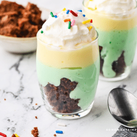 2 glasses filled with St. Patrick's Parfait and a cup of brownies cubed in the background
