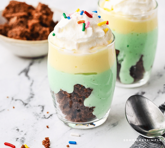 2 glasses filled with St. Patrick's Parfait and a cup of brownies cubed in the background