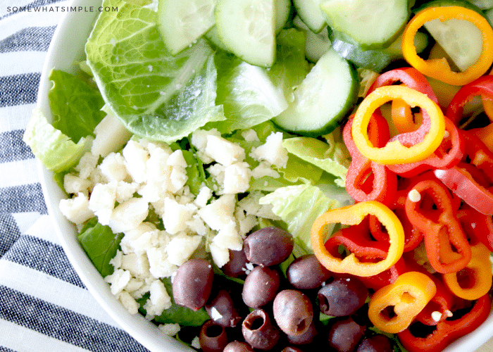 a salad with olives, peppers, cucumbers, cheese, and romaine lettuce