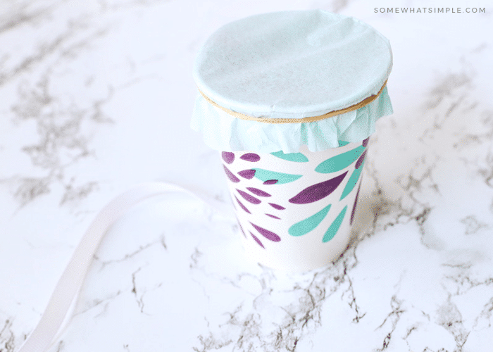 covering a paper cup with a piece of tissue paper and a rubberband