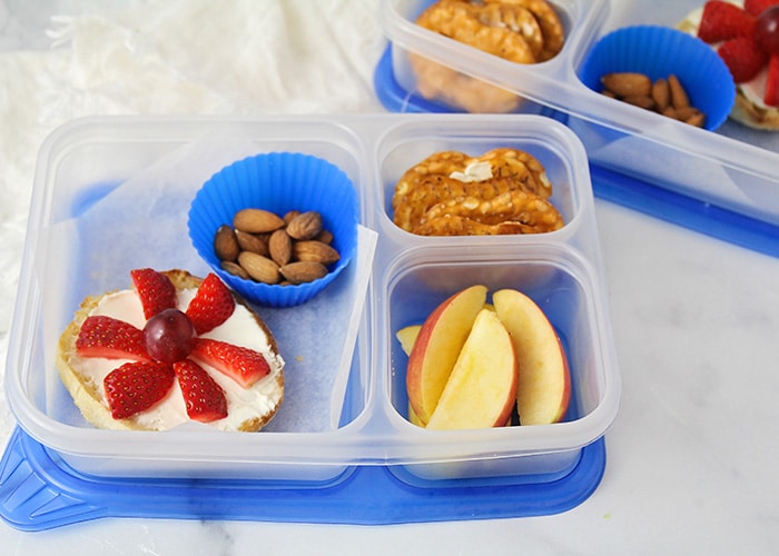 divided container with a bagel and cream cheese with apples and nuts