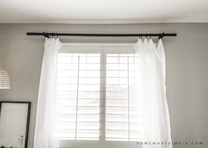 Open window with black curtain rod and white sheer curtains.