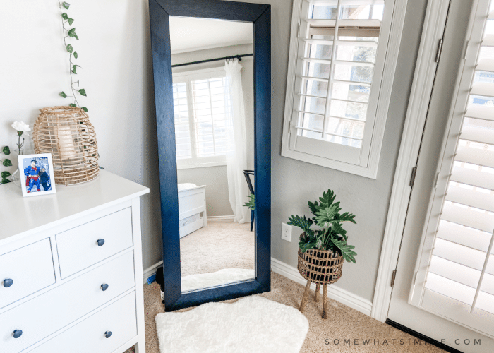 standing black mirror in the corner of a modern boho bedroom with a faux fur rug in front of it and a plant in a basket