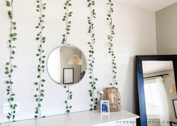 White dresser with green ivy hanging above it and a round mirror on the wall