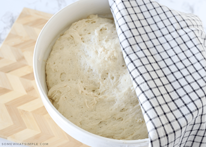 bowl of french bread dough, half covered by a towel