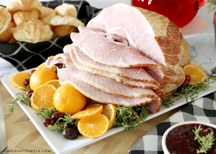 cooked ham sliced and sitting on a serving platter with pranges and rosemary